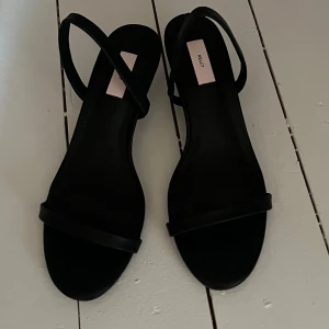 ”Klack” skor låg klack från Nelly, helt nya inte använda  - Från Nelly med smal rem över tårna och runt hälen. Skorna har en låg klack och öppen tå, perfekt för en trendig look. Tillverkade i syntetmaterial med minimalistisk design som passar till många outfits. Nypris: ca 200kr säljer för 90kr. Storlek 37 