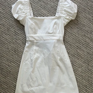 Vit kort puffärmad klänning Stradivarius - Superfin vit kort klänning från Stradivarius med puffärmar och fyrkantig ringning. Klänningen har markerad midja, rynkade detaljer vid axlar och rygg samt dragkedja bak. Perfekt för sommarens alla tillfällen!