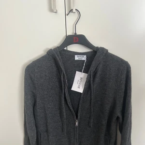 Grå kashmir hoodie från ROVOIR - Mysig grå hoodie från ROVOIR i 100% kashmir. Tröjan har dragkedja framtill, huva med snörning och långa ärmar. Perfekt för dig som gillar en stilren och lyxig look med maximal komfort. Lite liten i storleken så rekommenderar för XS