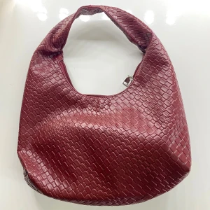 Vinröd axelväska i skinnimitation - Säljer en vinröd axelväska med snyggt ormskinnsmönster. Väskan har en mjuk, rundad form och stängs med dragkedja upptill. Perfekt storlek för att få plats med allt du behöver till vardagen.