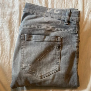 Dondup Jeans George - Säljer ett par ljusgrå skinny fit jeans från Dondup i modellen George. Klassisk femficksmodell med snyggt slitna detaljer på bakfickan. Jeansen har en smal passform och är tillverkade i mjukt denimtyg som sitter tajt men bekvämt.