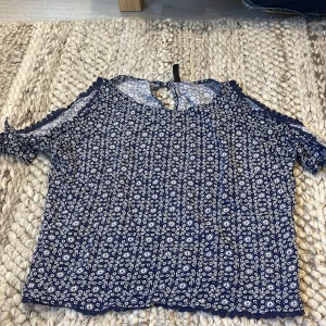 Blommig blå blus från H&M Divided - Supersöt blommig blus i marinblått och vitt från H&M Divided. Toppen har offshoulder-modell med knytband på ärmarna och små volangdetaljer längs kanterna. 