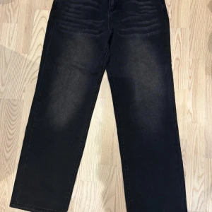 Svarta raka jeans med slitningar - Snygga svarta jeans med raka ben och diskreta slitningar över låren. Jeansen har en klassisk femficksmodell och är tillverkade i ett robust denimtyg. Perfekta för en avslappnad och cool stil.