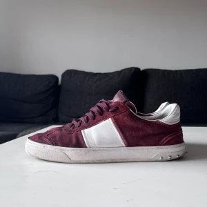 Valentino flycrew sneakers vinröd/vit - Snygga Valentino flycrew sneakers i vinrött mocka och vitt skinn. Klassisk låg modell med snörning och ikoniska nitar längs sulan. Perfekt för dig som vill sticka ut med exklusiva detaljer och cool färgkombo. Det är några få skador på den men lätta att fixa med rätt motivation har anpassat priset där efter. Dessa är mina favoriter men behöver pengarna till annat. Har inte låda då dom är köpte här på Plick. Det är inte vanligt för såhär ovanliga skor!