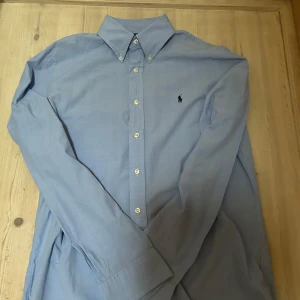 Blå slim fit skjorta från Ralph Lauren S - Klassisk ljusblå skjorta från Ralph Lauren i slim fit-modell. Skjortan har vita knappar och svart logga. Tillverkad i bommul och jag tror den är i S.