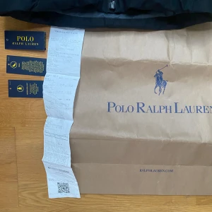 Polo Ralph Lauren Dunjacka - Snygg svart dunjacka från Polo Ralph Lauren i storlek XS. Jackan har en klassisk pufferstil med huva, dragkedja framtill och en röd detalj på ärmfickan. Broderad logga på bröstet och flera praktiska fickor. Perfekt för kalla dagar och riktigt stilren look. Nypris: 5495kr. Marinblå/svart. OBS - priset är högt på grund av plicks nya system med deras avgift de tar. Billigare på vinted.