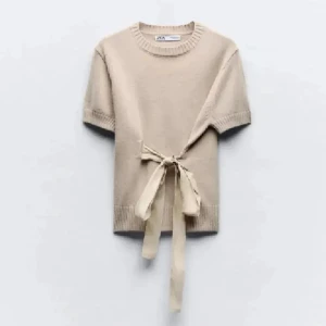 Beige stickad tröja med knyt från Zara - Superfin beige stickad tröja från Zara med korta ärmar och snygg knytning i midjan. Perfekt för dig som gillar en enkel men ändå unik look. Tröjan har rund halsringning och ribbade detaljer vid ärmslut och nederkant.