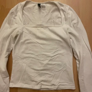 Vit långärmad topp med fyrkantig ringning - Säljer en stilren vit långärmad topp från H&M med snygg fyrkantig ringning. Toppen är i mjuk bomull och har en figurnära passform som passar perfekt till jeans eller kjol. Enkel och clean look som funkar året runt.