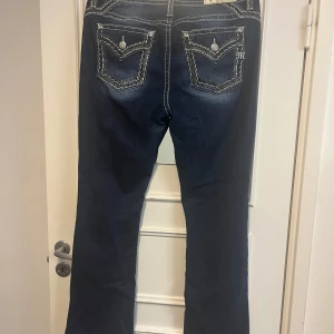 Miss Me bootcut jeans med broderi - Snygga mörkblå bootcut jeans från Miss Me med kontrastsömmar och broderade detaljer på bakfickorna. Jeansen är i storlek 31, och är lite slitna i ändarna.