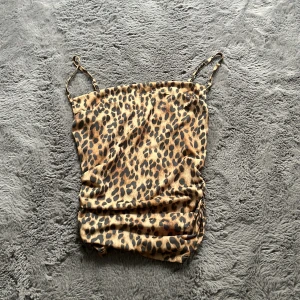 Leopardmönstrad linnetopp Divided - Säljer en leopardmönstrad linnetopp från Divided i storlek XXS. Toppen har tunna axelband och snygg rynkdetalj på sidan. Färgerna går i brunt, beige och svart och materialet är mjukt och stretchigt. Perfekt för dig som vill sticka ut med ett djurmönster! Köpt på H&M för över 1 år sen och är osäker om den säljs längre. Använd 1 gång och är i perfekt skick.