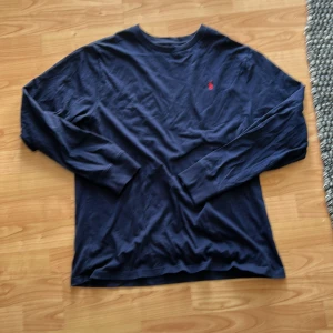 Mörkblå långärmad tröja Polo Ralph Lauren - Snygg mörkblå långärmad tröja från Polo Ralph Lauren i bomull. Klassisk crewneck med röd broderad logga på bröstet. Perfekt för dig som gillar stilrena och tidlösa plagg. Passar till jeans eller chinos för en clean look. Aldrig använd.