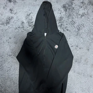  Moncler hoodie - Svart hoodie från Moncler med klassisk logga på bröstet. Tröjan har huva med snörning, hel dragkedja framtill och känguruficka. Tillverkad i mjuk bomull, perfekt för chill dagar. Långärmad och stilren design som funkar året runt. 
