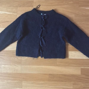 Svart kofta med snörning från Gina Tricot - Mysig svart kofta från Gina Tricot i stickat material. Koftan har långa ärmar och snygg snörning framtill istället för knappar. Perfekt för lager-på-lager och ger en chill vibe till din outfit.