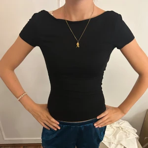 Svart topp med öppen rygg - Snygg svart topp med tight passform och korta ärmar. Toppen har en cool öppen rygg som ger en unik look. Perfekt för dig som vill sticka ut lite extra. Enkel och stilren framtill, men med en oväntad twist bak.