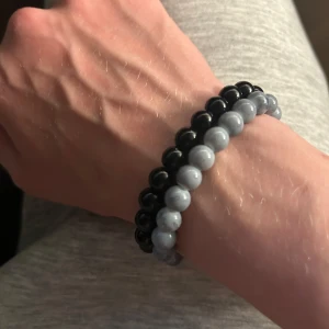 Två pärlarmband i svart och grått - Säljer två stilrena armband med runda pärlor, ett i svart och ett i ljusgrått. Perfekta att bära tillsammans eller var för sig för en clean look. Elastiska och enkla att ta på. Passar både tjejer och killar som gillar minimalistiska accessoarer. Passar 15-17cm handled och pris är förhandlingsbart🙌