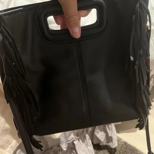 Svart axelväska med fransar - Säljer min fina maje väska i stl stor  ! Den använd ett par gånger, det är en äkta men maje texten är borta! Axelband ingår, tryck inte på köp nu är inte hemma och säljer ngn annan stans oxå! Kp för bilder eller frågor❤️