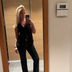 Svart klassisk väst med knappar - Stilren svart väst med v-ringning och knäppning framtill. Västen har en klassisk passform och är ärmlös, perfekt att styla över en skjorta eller t-shirt. Enkel och tidlös design som funkar till många olika looks. Endast använd 2 gånger så den är för liten! Skit snygg😍