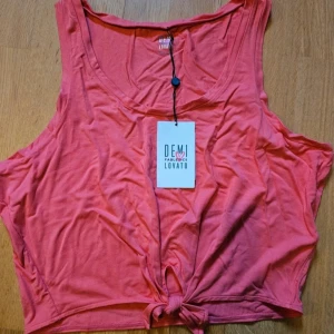 Rosa linnetopp från Fabletics Demi Lovato - Snygg rosa linnetopp från Fabletics Demi Lovato-kollektionen. Modellen är ärmlös med rundad halsringning och en knutdetalj framtill. Tillverkad i mjuk och stretchig bomullsjersey som känns skön mot huden. Perfekt för dig som gillar en avslappnad och trendig look.