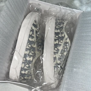 Dior Granville sneakers grå broderade - Snygga Dior Granville sneakers i grått med broderat Dior Oblique-mönster. Skorna har vita snören, rund tå och platt sula. Märkeslogga på plösen och sidan. Perfekta för dig som vill ha en lyxig och trendig look.