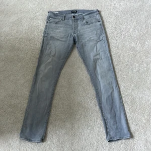 Grå slim jeans Jack & Jones  - Snygga ljusgrå slim fit jeans från Jack & Jones, modell Slim Glenn. Klassisk femficksdesign, smal passform och tillverkade i mjukt bomullsmaterial med  stretch. Perfekta för en clean och modern look. W34 x L32