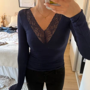 Mörkblå långärmad topp med spets - Supersnygg mörkblå långärmad topp från Gina Tricot med djup v-ringning och spetsdetaljer framtill. Tight passform som framhäver figuren och mjukt bomullsmaterial som känns skönt mot huden. Perfekt att styla med jeans eller kjol. Använd fåtal gånger, inga defekter🌸