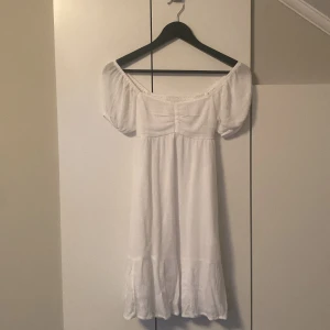 Vit offshoulder klänning Hollister - Superfin vit kortklänning från Hollister med offshoulder och puffärmar. Klänningen har en öppen rygg och volang nertill, perfekt för sommarens varma dagar. Lätt och luftig i bomull, ger en romantisk vibe.har använt en gång på skolavslutningen 💞