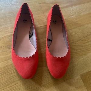 Röda ballerinaskor från H&M, stl 38 - Obs färgen är mer lik den på första bilden💕Snygga röda ballerinaskor från H&M i mockaimitation med vågig kant runt öppningen. Skorna har rund tå och platt sula, perfekta för dig som vill ha en poppig färg på fötterna. Enkla att matcha och superbekväma att bära hela dagen.