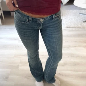 True Religion bootcut jeans blå - Säljer ett par klassiska blå jeans från True Religion med bootcut passform. Jeansen har låg midja, snygga kontrastsömmar och ikonisk patch bak. Jeansen är väldigt stretchiga så de kan passa M och L