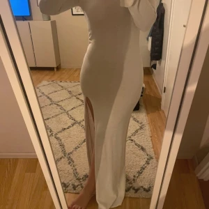 Lång vit klänning med slits - Supersnygg lång vit klänning med lång ärm och hög slits på ena sidan. Klänningen har en tight passform och öppen rygg med fyrkantig urringning. Perfekt för dig som vill sticka ut med en stilren och elegant look.