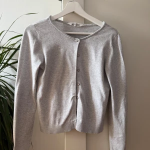 Grå kofta från H&M - Säljer en söt grå kofta från H&M med rund halsringning och knäppning framtill. Säljer pga den blev för liten. 