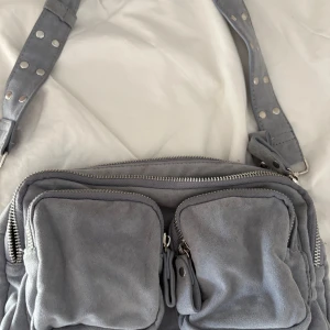 Grå/blå mocka axelväska från Gina Tricot - Super snygg handväska från Gina tricot, väskan är nästan aldrig använd och är i ett mycket bra skick, hör av er för fler frågor priset kan diskuteras vid snabb affär🩷