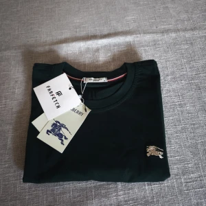 Mörkgrön Burberry t-shirt - Snygg mörkgrön t-shirt från Burberry med klassisk rund hals och liten broderad logga på bröstet. Tillverkad i mjuk bomull med lite stretch för extra komfort. Storlek S. Ny med lapp.