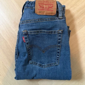 Levi's 501 blå jeans - Klassiska blå Levi's 501 jeans med rak passform och ikonisk röd etikett på bakfickan. Jeansen har fem fickor, knappgylf och är tillverkade i slitstarkt denim. Perfekta för dig som gillar tidlös stil och vill ha ett par riktigt snygga jeans.