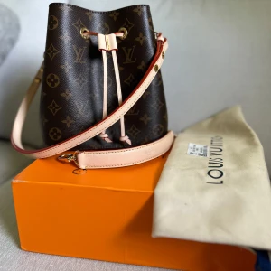 Bucket bag - Säljer en klassisk brun axelväska med ikoniskt monogrammönster och snygga ljusa skinnremmar. Väskan har dragsko upptill och guldiga detaljer. Perfekt för dig som vill ha en lyxig och tidlös accessoar. Väskan var en gåva, osäker på äktheten och därav lågt pris. 