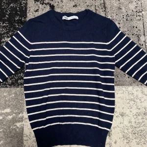 Randig marinblå tröja från Zara - Snygg marinblå tröja från Zara med vita horisontella ränder. Tröjan har rund halsringning, 3/4 ärmar och är tillverkad i ett mjukt, stickat material. Perfekt för dig som gillar klassisk och stilren look.