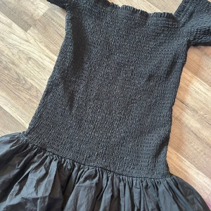 Svart smockad klänning från H&M - Supersöt svart klänning från H&M med smockad överdel och volangig kjol. Offshoulder-modell. Knappt använd så inga defekter. Skriv för intresse.💕