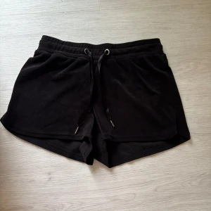 Svarta mjuka shorts med snörning - Svarta shorts i mjukt frottéliknande material med elastisk midja och snörning framtill. De har en avslappnad passform och är perfekta för chill dagar eller träning. Klassisk design utan mönster eller extra detaljer. Shortsen är från Gina Tricot.