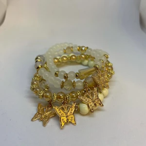 Guldiga armband med fjärilar - Flera elastiska armband i vitt och guld med pärlor och glittriga detaljer. Varje armband har hängen i form av guldiga fjärilar som ger en söt och trendig look. Ej använd utan kommer från min small business. Fri frakt kan jag lösa.