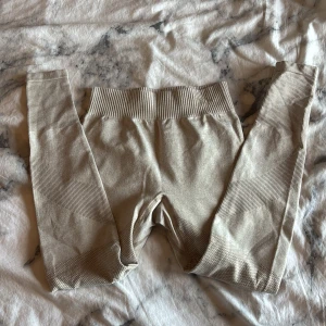 Beige seamless leggings från lager 157 - Snygga beige seamless leggings från lager 157 med hög midja och ribbade detaljer längs midjan och benen. Stretchigt material som sitter tight och formar sig efter kroppen, perfekta för träning eller chill. Diskret logga framtill. Storlek 130/140