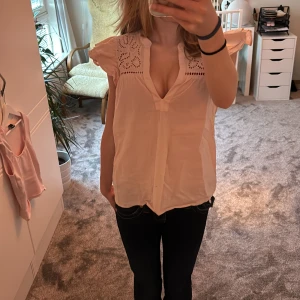 Ljusrosa blus med broderade detaljer - Supersöt ljusrosa blus från H&M med broderade detaljer upptill och djup v-ringning. Blusen har volangiga korta ärmar. Snygg och luftig passform. Nypris 199kr