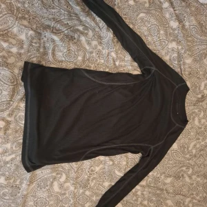 Svart långärmad tröja i ullmix - En svart långärmad tröja i tunn ullmix med diskreta sömmar. Perfekt som baslager under kalla dagar. Tröjan har en enkel och stilren design med rund hals och smal passform.