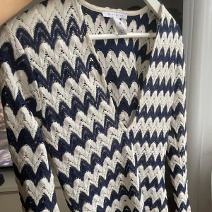 Mönstrad kortklänning från NLY Trend - Kort beachklänning från NLY Trend med vit och marinblå zickzack-mönster. Klänningen har lång ärm, v-ringning och är stickad i ett luftigt material. 