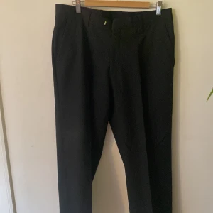 Svarta kritstrecksrandiga kostymbyxor från Batistini - Snygga svarta kostymbyxor från Batistini med tunna vita ränder för en klassisk pinstripe-look. Byxorna har raka ben, bälteshällor och diskreta bakfickor. Perfekta för dig som vill ha en stilren och dressad vibe.                 Strl- 97/82 ( ca L)