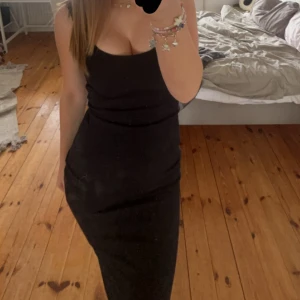 Svart tight långklänning - Säljer en svart långklänning med smala axelband och figurnära passform. Klänningen är ärmlös och har en enkel, stilren design som framhäver siluetten. Perfekt för dig som gillar minimalistisk och klassisk stil.