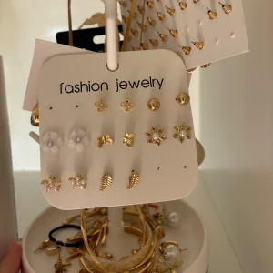 Mix av örhängen i guld och vitt - Säljer ett stort set med örhängen i olika former och storlekar, mestadels i guldton med inslag av vitt och pärlor. Här finns blommor, löv, hoops och studs – perfekt för dig som vill variera din stil. Materialet är metall och plast, vissa med pärldetaljer. Ringar och några armband samt smyckesträdet ingår. Säljer för att jag insett att jag är mer silver än guld! 50kr för ALLT. Allt är från SHEIN 