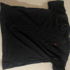 Svart t-shirt Polo Ralph Lauren - Svart t-shirt från Polo Ralph Lauren i bomull med klassisk passform. Liten röd broderad logga på bröstet. Enkel och stilren design med korta ärmar och rund hals. Perfekt för en clean och avslappnad look.