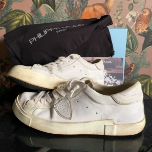 Vita Philippe Model  - Snygga vita sneakers från Philippe Model med klassisk låg profil och rund tå. Skorna har snörning, diskret logga på sidan och detaljer i skinn och textil. Perfekta för en clean och stilren look. Kommer med originalkartong och dustbag. Storlek 42. Skriv vid funderingar om vad som.