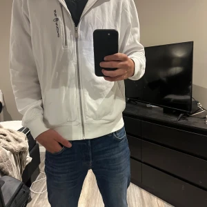 Sail Racing zip hoodie vit - Sail Racing zip hoodie vit.                                                  Tyvärr lite skadad vit ändan på armen men annars toppskick👌🏼