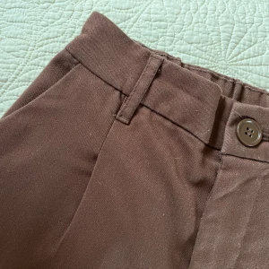 Bruna kostymbyxor - Mörkt kastanjebruna kostymbyxor från HM Divided. Högmidjade och raka med så härliga, flowy ben och mjuka med bekvämt resår i midjan. Ger en sådan höstig känsla med en stickad tröja eller skjorta till! Säljer pga att de blivit för små. Tyget är lite nopprigt på sina ställen, men inget jag stört mig på. 