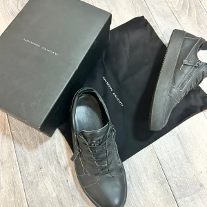 Svarta sneakers från Giuseppe Zanotti - Snygga svarta sneakers från Giuseppe Zanotti i skinn med coola dragkedjor på sidorna och snörning framtill. Skorna har använts ett tagg och är i storleken 44, priset går att diskutera!! har inget kvitto eller bevis på köp då jag ärvt dessa skor